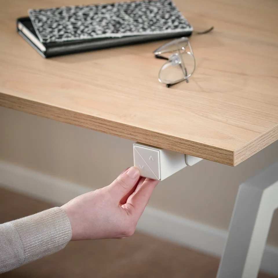A hand adjusts a sit-stand desk button, demonstrating its height adjustment feature.
