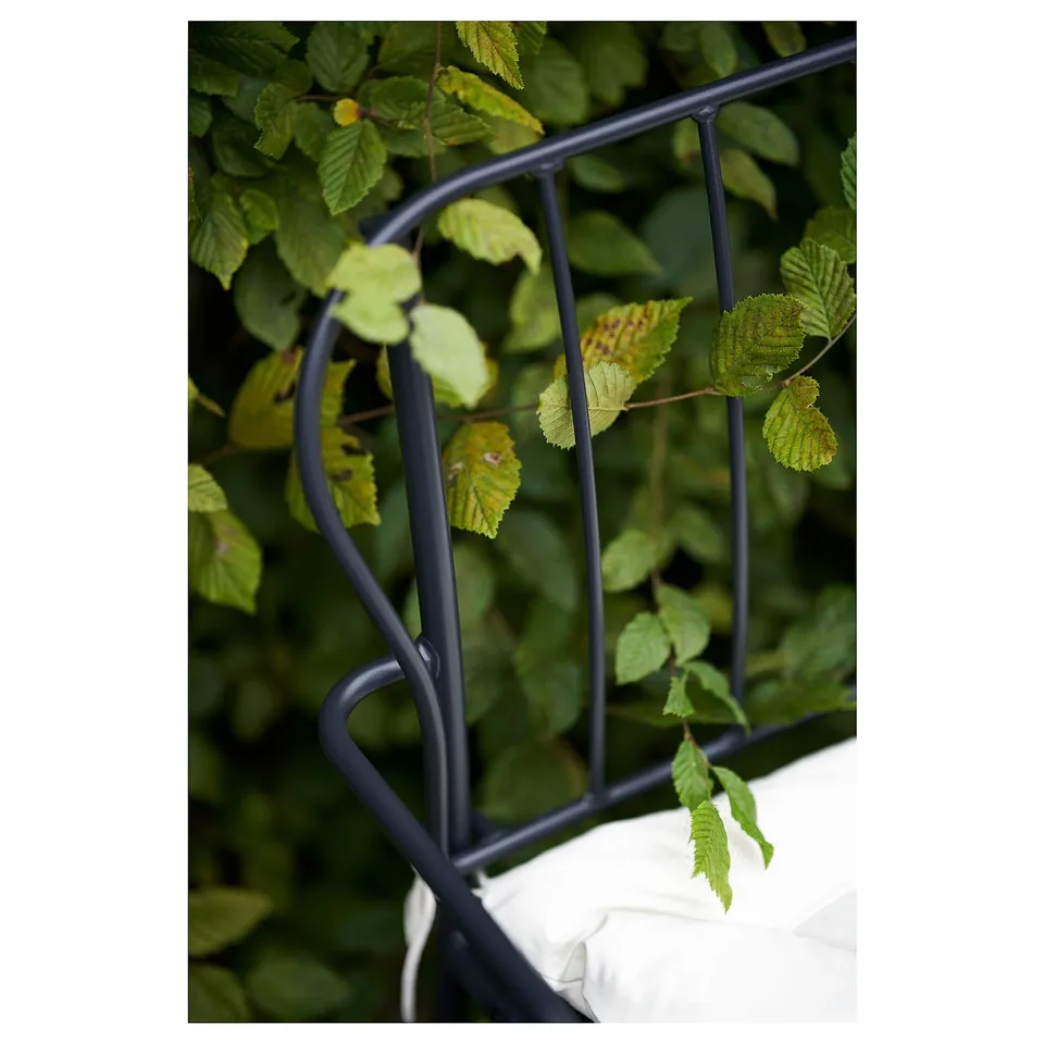 Black metal trellis with green leaves growing through it.