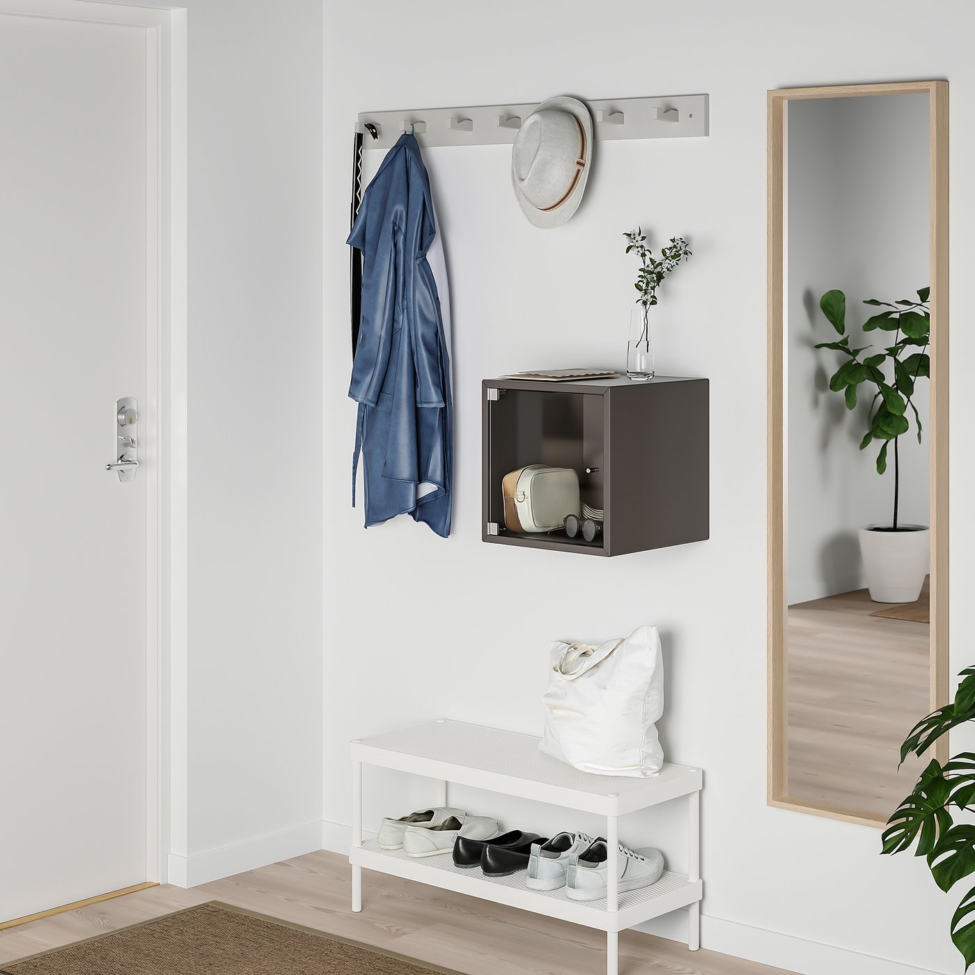 Small brown EKET cube hangs on wall, storing bag near white shoe rack with blue coat and hat above.