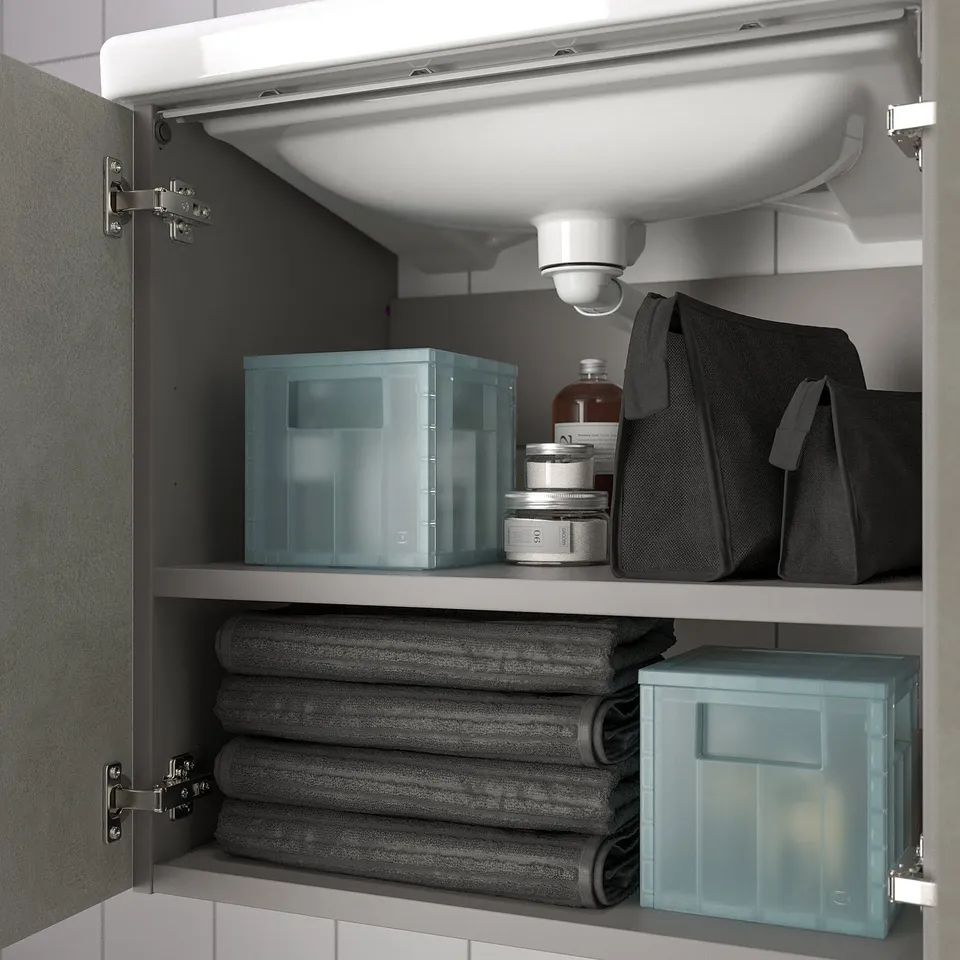 Under-sink cabinet with two shelves, neatly organised bathroom items including stacked towels and blue storage boxes for toiletries.