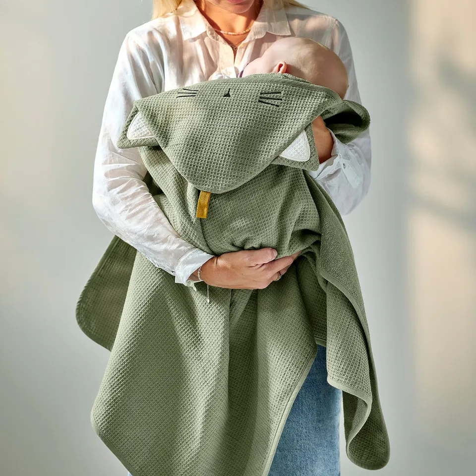 A person holding a baby wrapped in a green hooded towel with waffle texture, featuring a loop for hanging.