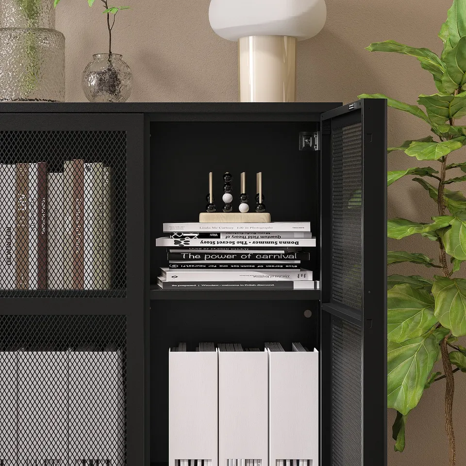 Black metal cabinet with mesh doors on wall, storing books and accessories.
