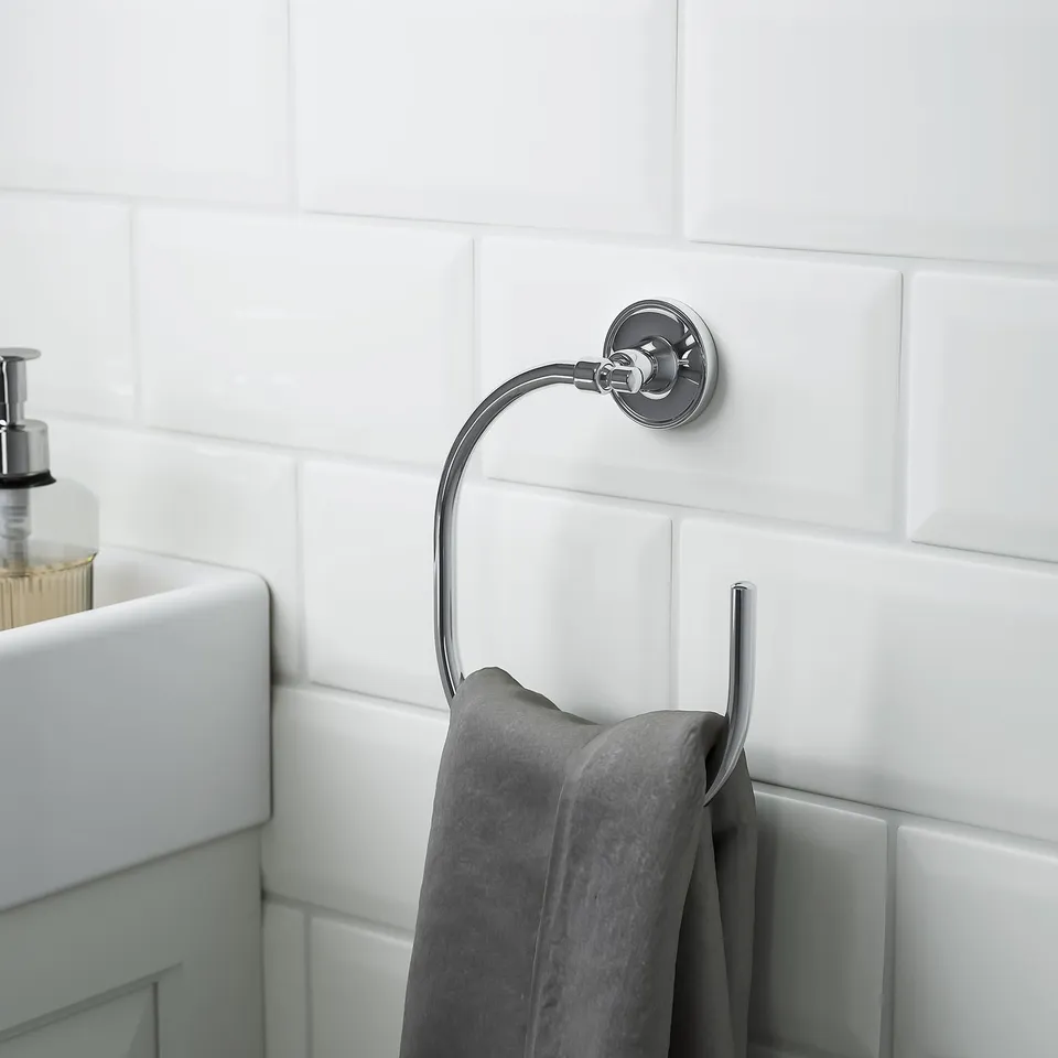 Chrished metal towel ring holds grey towel, mounted on tiled wall near sink.