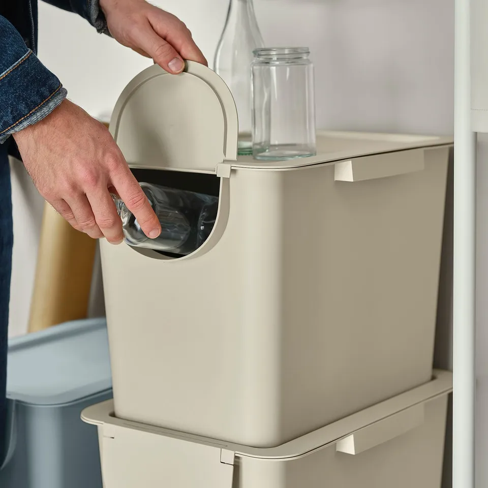 Person opens rubbish bin with lid. Adjustable waste sorting in stylish, stackable design.