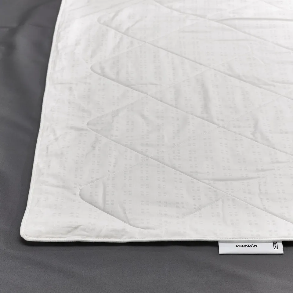 Close-up of a white silk-filled duvet on a dark background, showcasing its soft, luxurious texture. Ikea label visible.