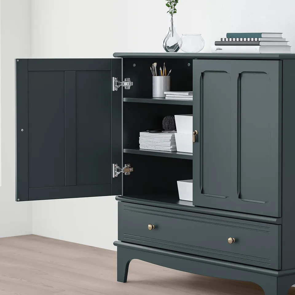 Dark green LOMMARP cabinet with open doors reveals shelves holding books and supplies; top holds decorative vases and books.