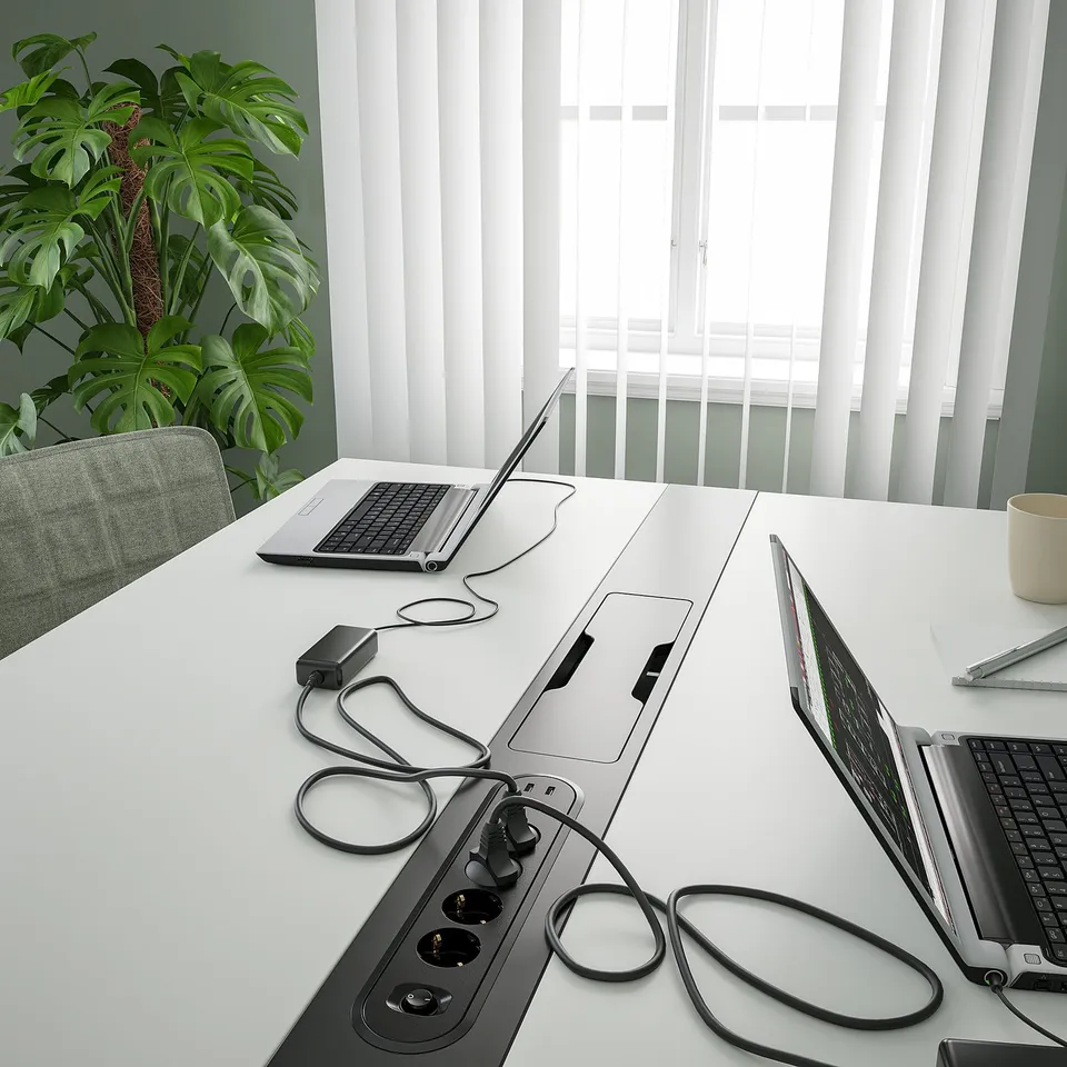 Modern white conference table with built-in power outlets and cable management, laptops and plant on surface.