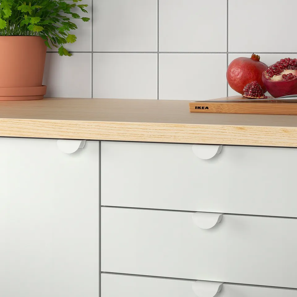 Wood countertop with white cabinets, featuring clip-on handles, and a pomegranate on a cutting board.