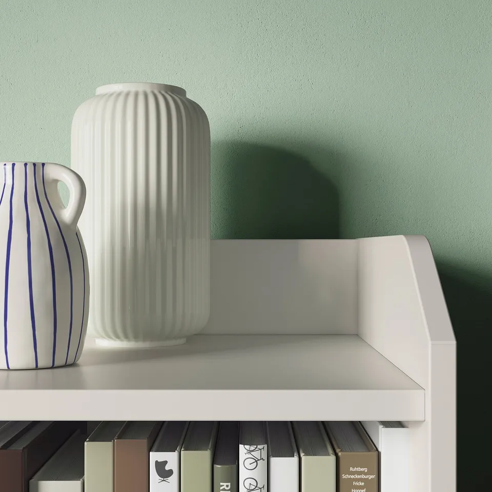 Two white vases, one ribbed, one striped, on a white shelf against a green wall.