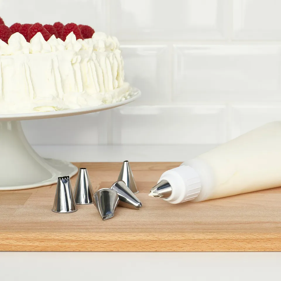 Silicone piping bag with metal tips on a wooden table, next to a frosted cake with berries on top.