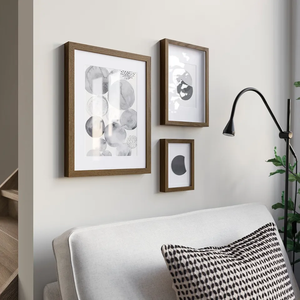Three RÖDALM frames with modern art prints above grey sofa. Black wall lamp and plant to right. Cosy, stylish decor.