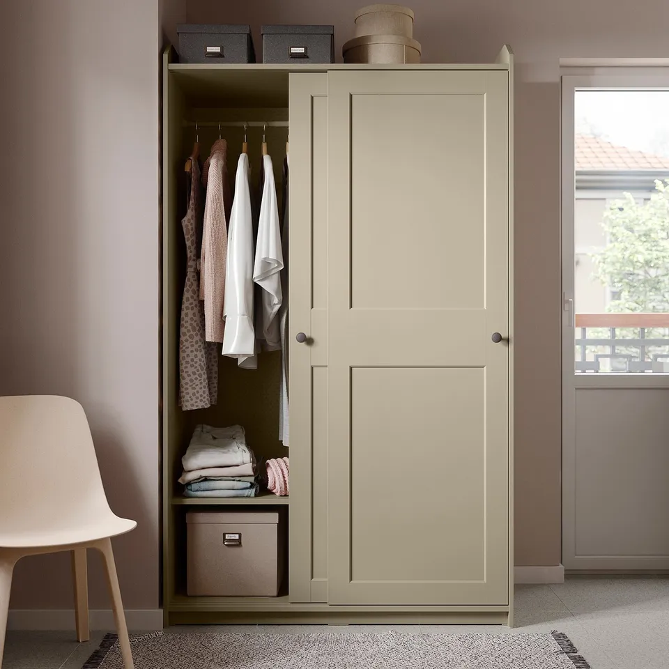Beige HAUGA wardrobe with sliding doors, both hanging and shelves, in a room with a white chair.