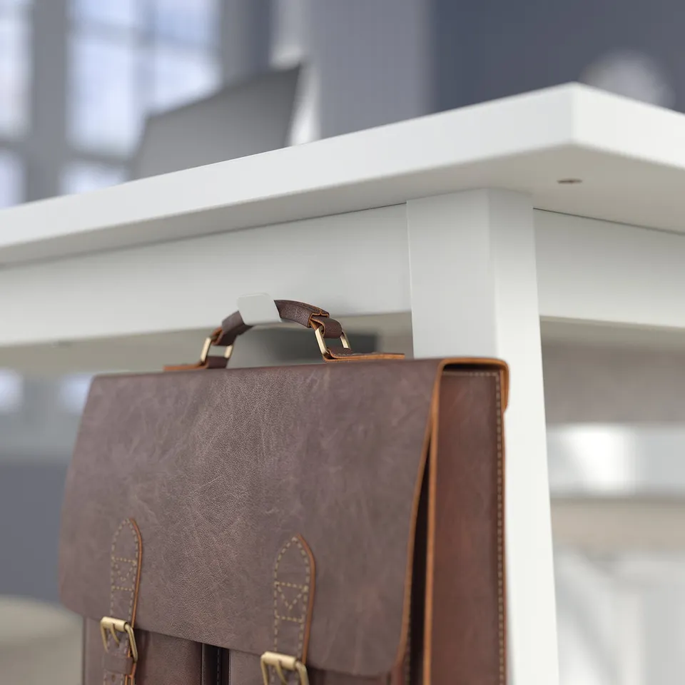 Brown leather bag hangs on white office table with cable management slot.