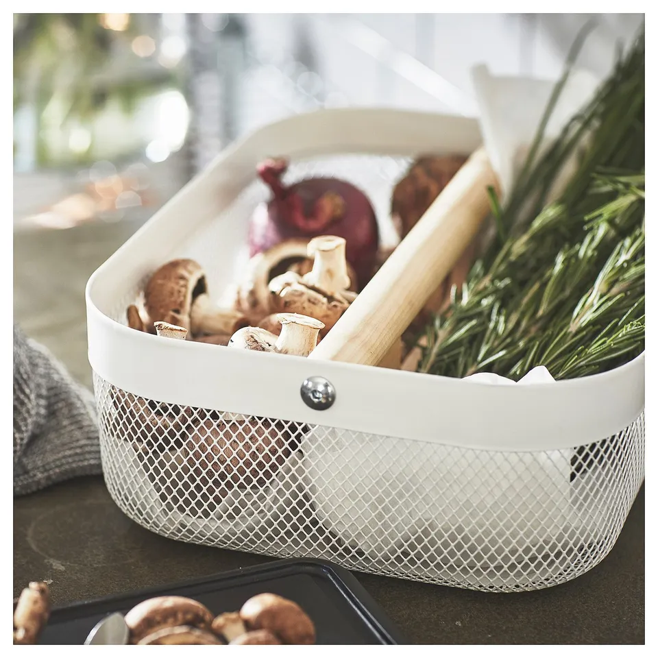 White RISATORP storage bin with mesh design, containing mushrooms, onion, and herbs, has a handle for easy transport.
