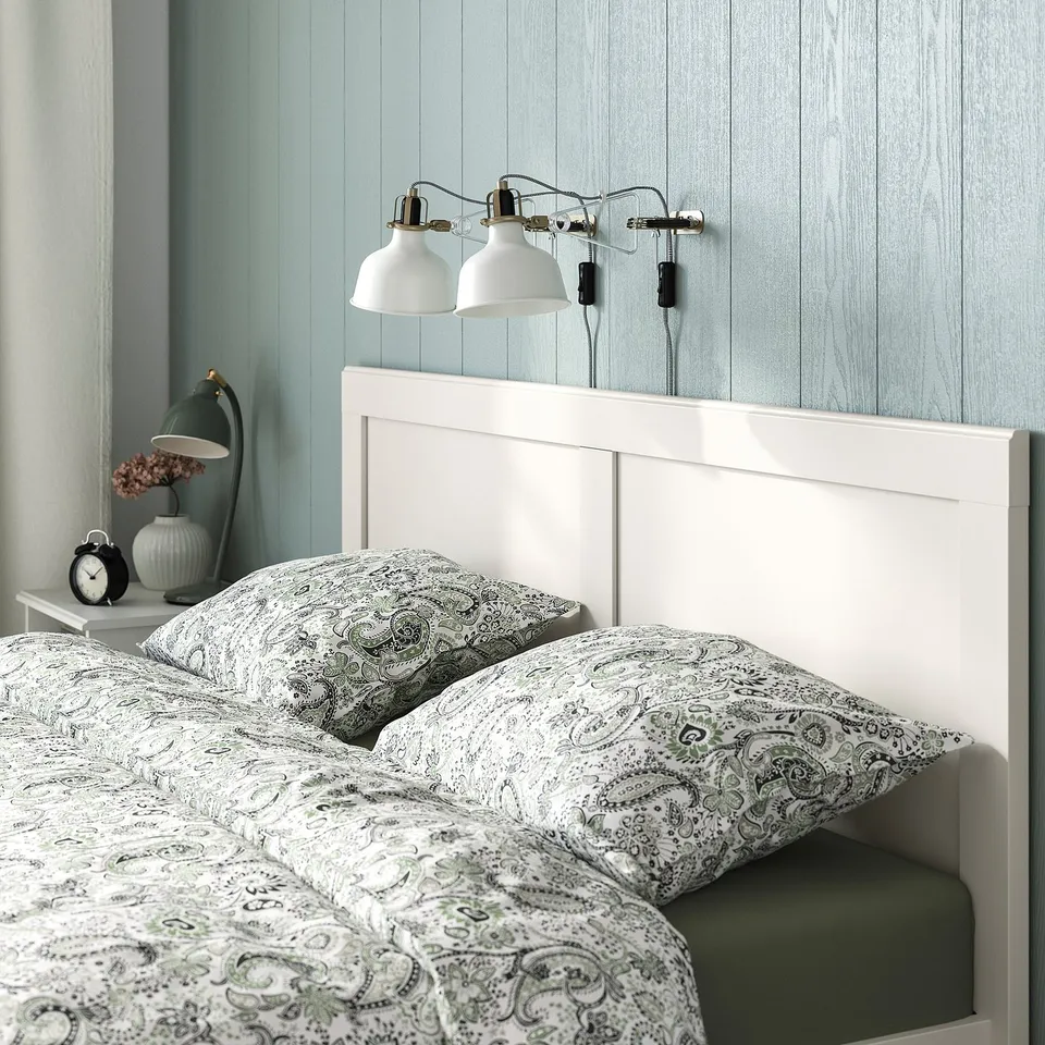 Bedroom with white bed, green wall, two lamps.