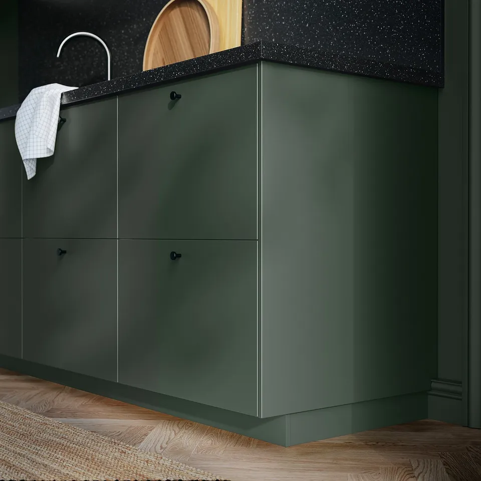 Green kitchen cabinet with black countertop and white sink.