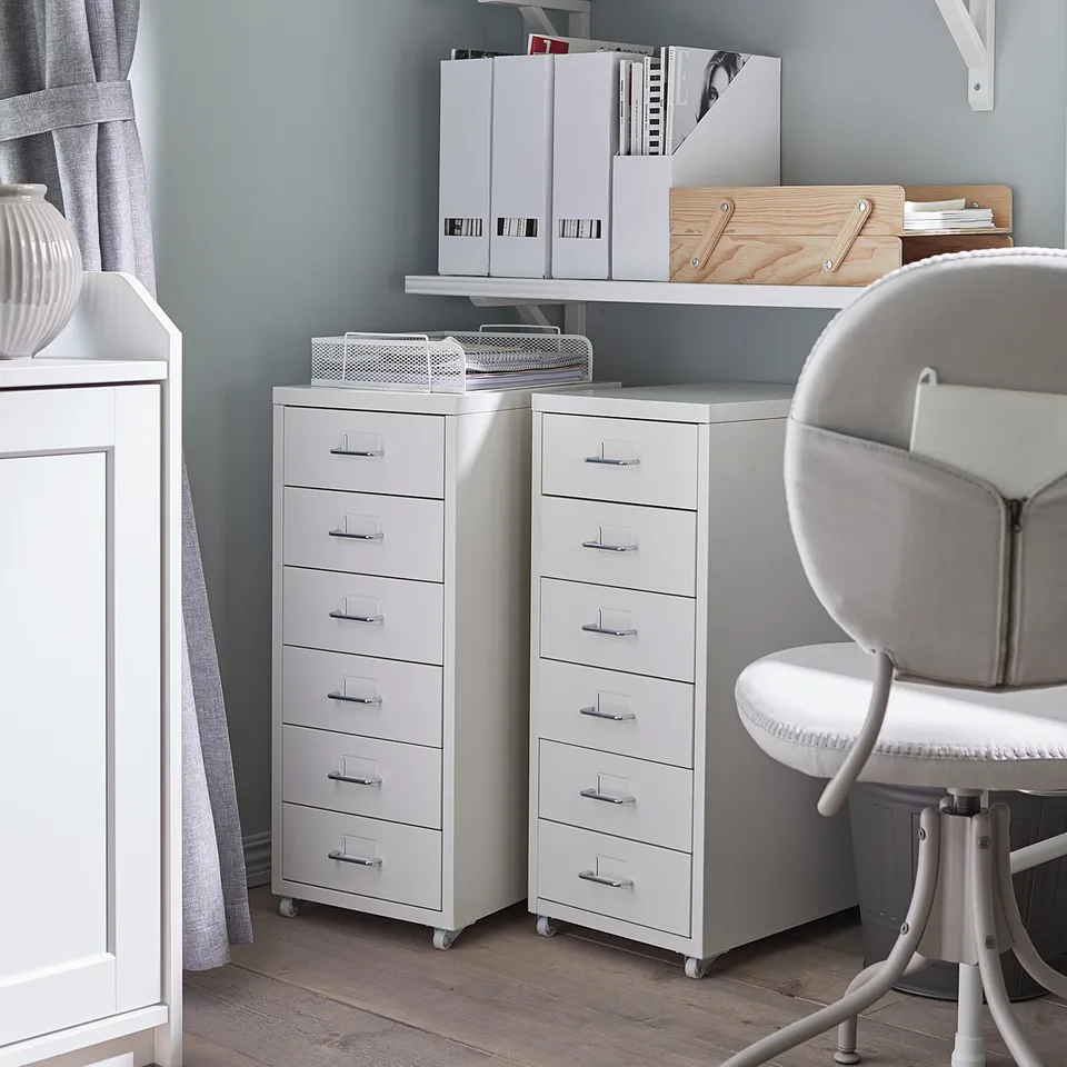 Well-organized home office with white HELMER drawer units on wheels. Multiple drawers, shelves, and a grey swivel chair. Grey walls and wooden floor.