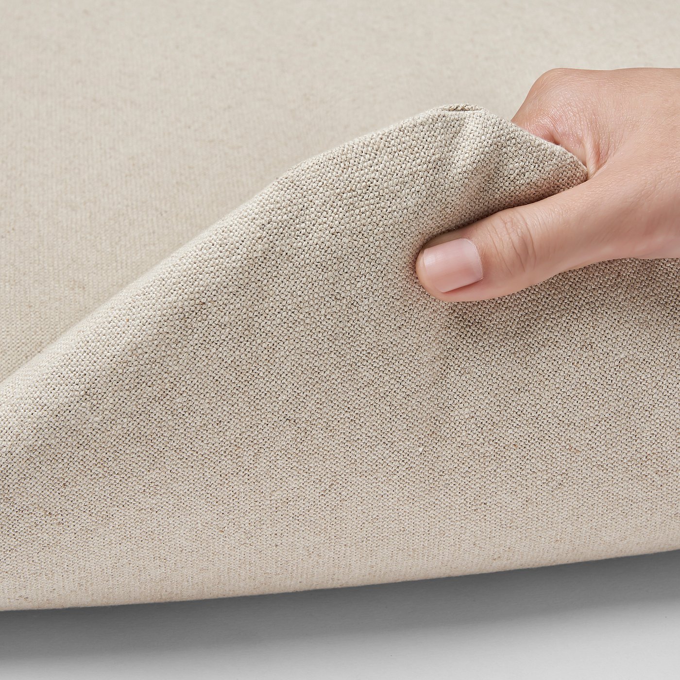 Image shows hand holding beige fabric, showcasing its soft texture and durability.