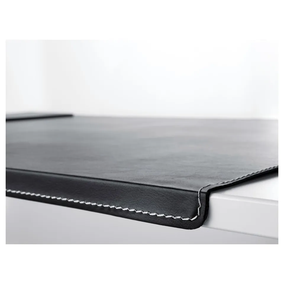 Close-up of a black desk pad with stitched edges on a white desk showing its smooth texture and quality finish.