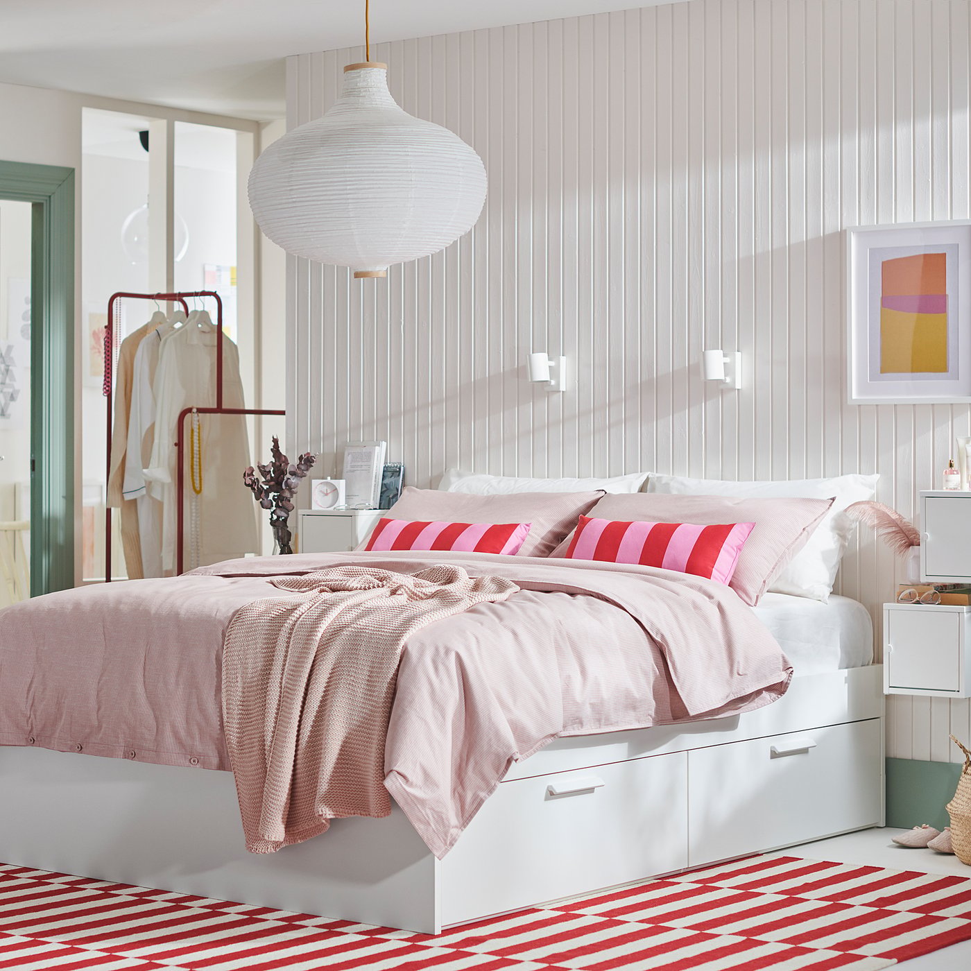 Bedroom with white BRIMNES storage bed, light pink bedding, red striped rug. Large white pendant lamp hangs above.