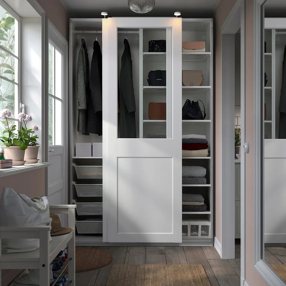 Open PAX wardrobe with clothes, glass doors, neat organisation in a cosy room.