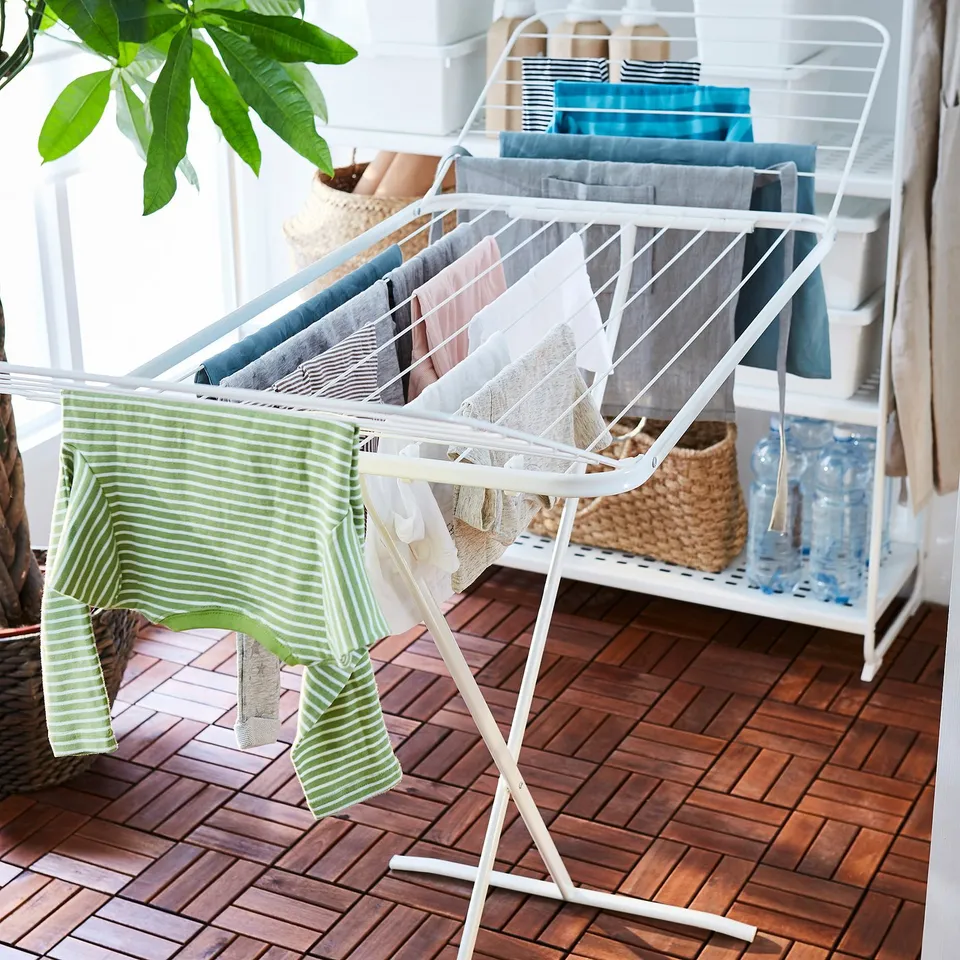 White indoor-outdoor drying rack with fold-out wings holding colourful clothes, featuring hooks for smaller items like socks.