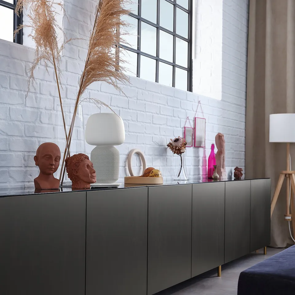 Modern room with grey ÖSARP unit, gold legs, decor on top, white brick wall, black bed.