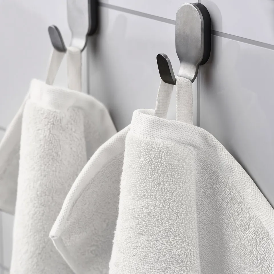 Three organic cotton towels on modern hooks, grey wall.