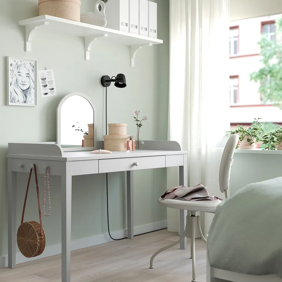 Modern room with SMYGA desk, chair, mirror, and shelves. Decorated with art, plants, and a bag; natural light from a large window.