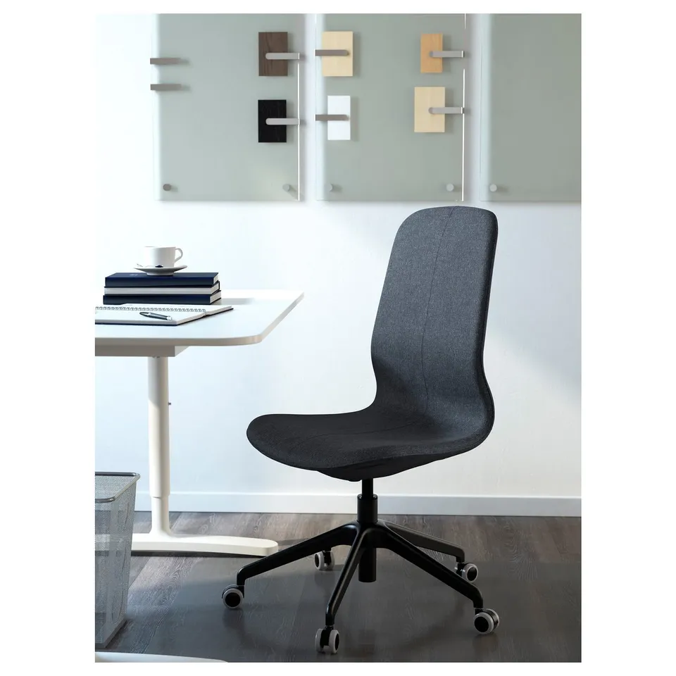 Modern office chair with adjustable height, lumbar support, and wheels, positioned near a white table with books and coffee cup.