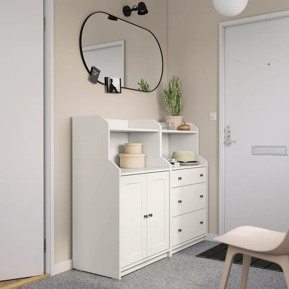Modern entryway featuring a white HAUGA storage unit with drawers and shelves, topped with a round mirror and decorative plants.