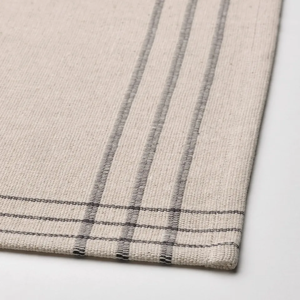 Beige and grey striped dining mat, woven from cotton and jute, laid on a table.