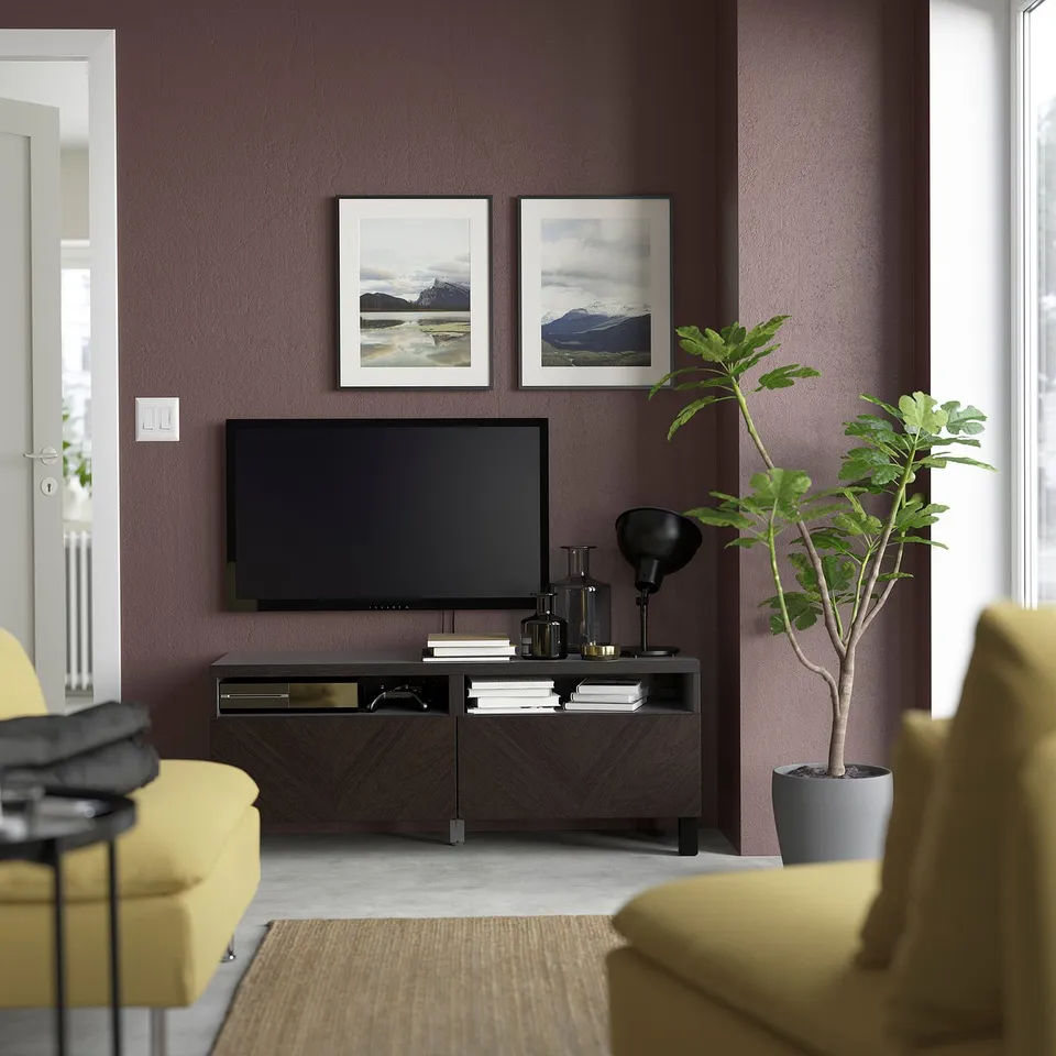 Modern living room with purple walls, tv on brown BESTÅ, flanked by yellow chairs, mountain photos, green plant.