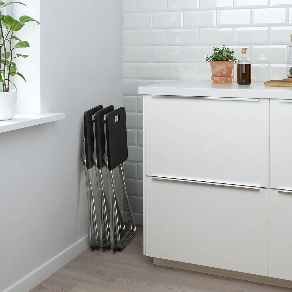 Foldable stools stored against clean, white kitchen counter. Ideal for extra seating or saving space.