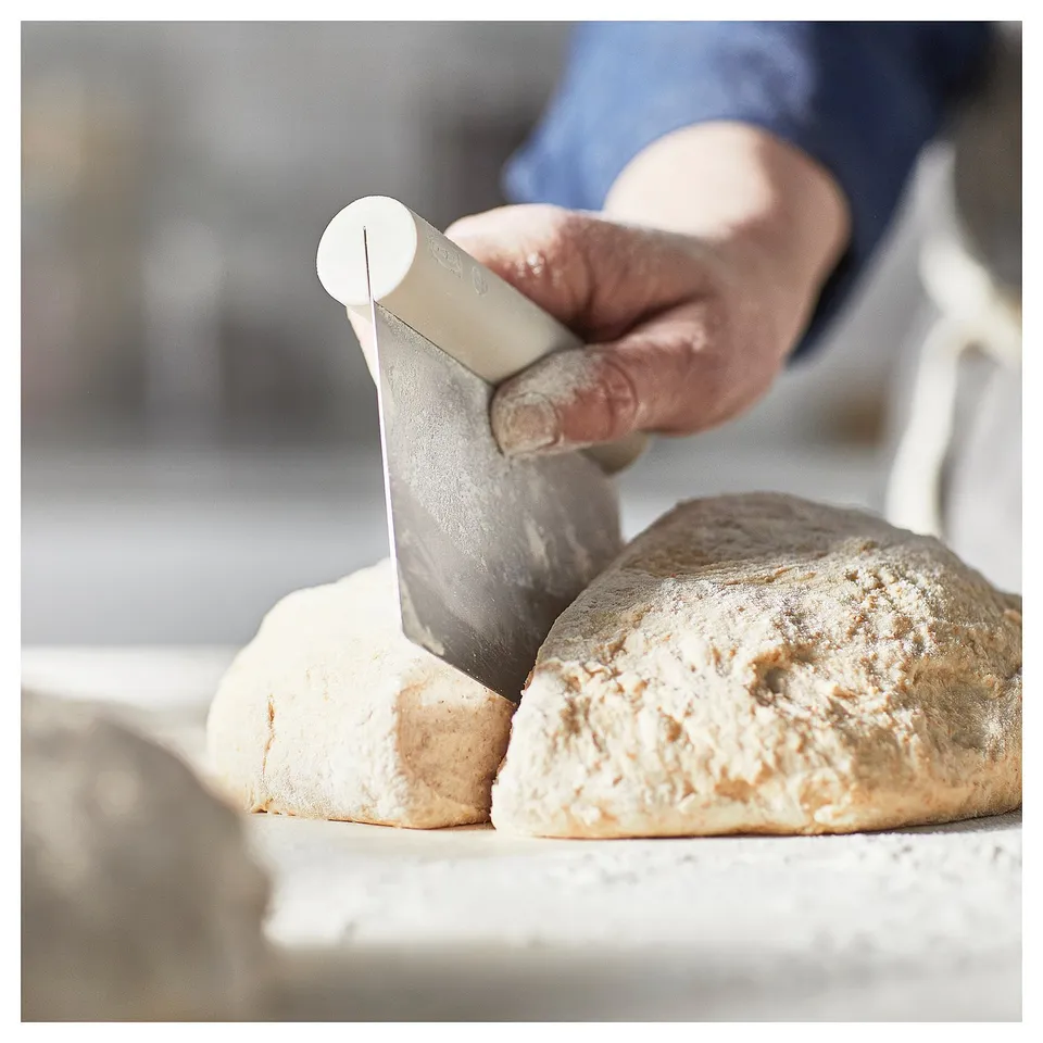 Hand cuts brown bread on white board.