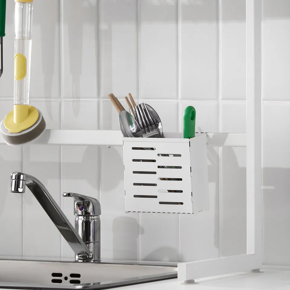 Kitchen sink with a white SKYGGFISK dish drainer, holding utensils and a green sponge on the tap.