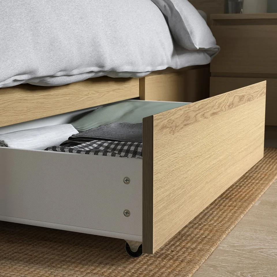 Wooden bed with open drawer showing neatly folded clothes, highlighting practical storage space.