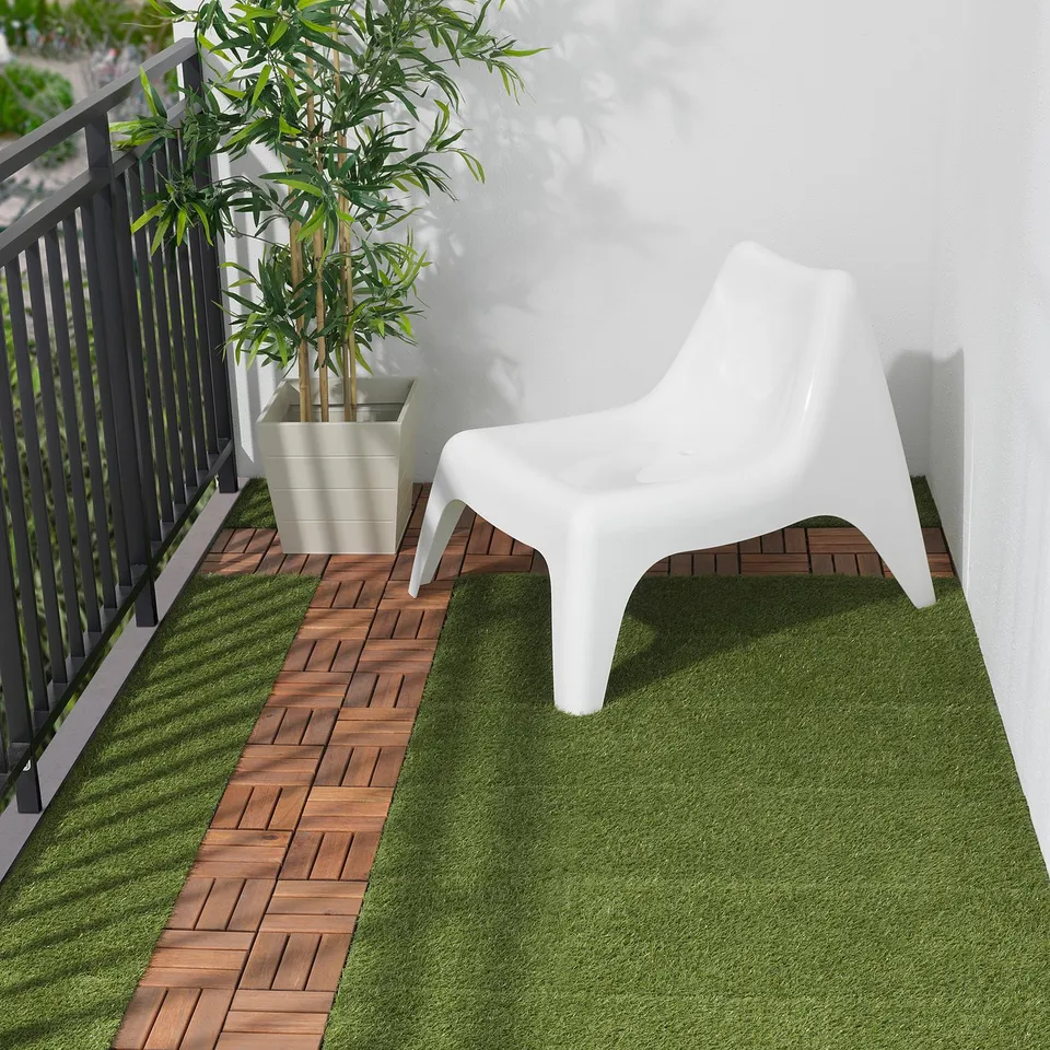 Small, white RUNNEN plastic chair on grassy balcony, next to potted plant.