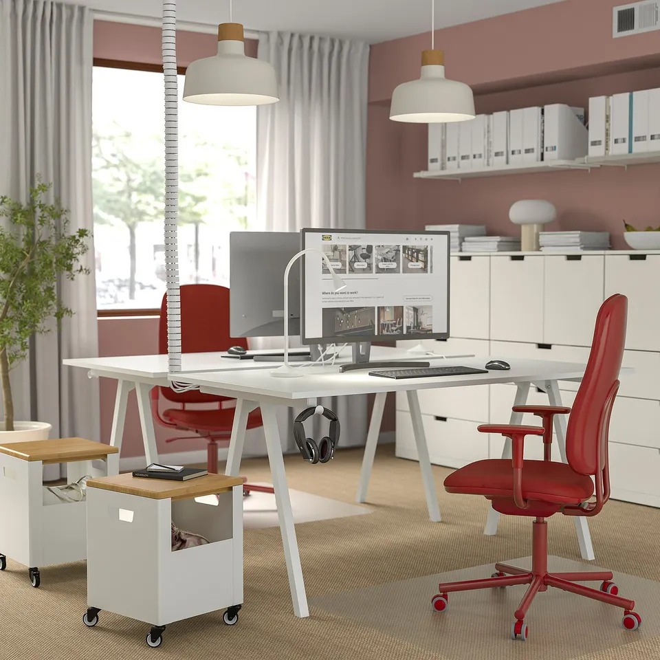 Modern office with white desks, red chairs. Large monitor, headphones. Bright, spacious, well-lit.