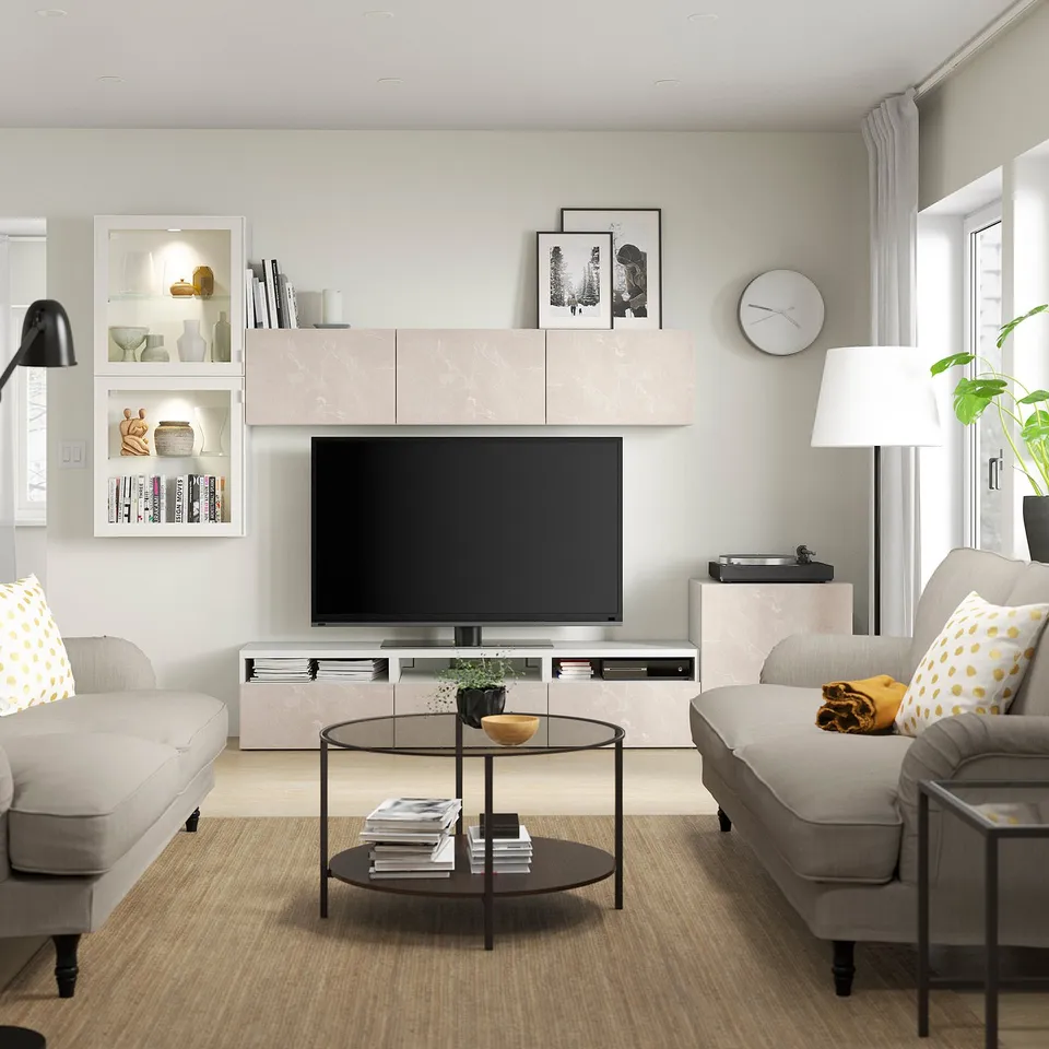 Modern living room with BERGSVIKEN beige marble tv stand, kallax shelves, grey couches, round glass coffee table, and large windows.