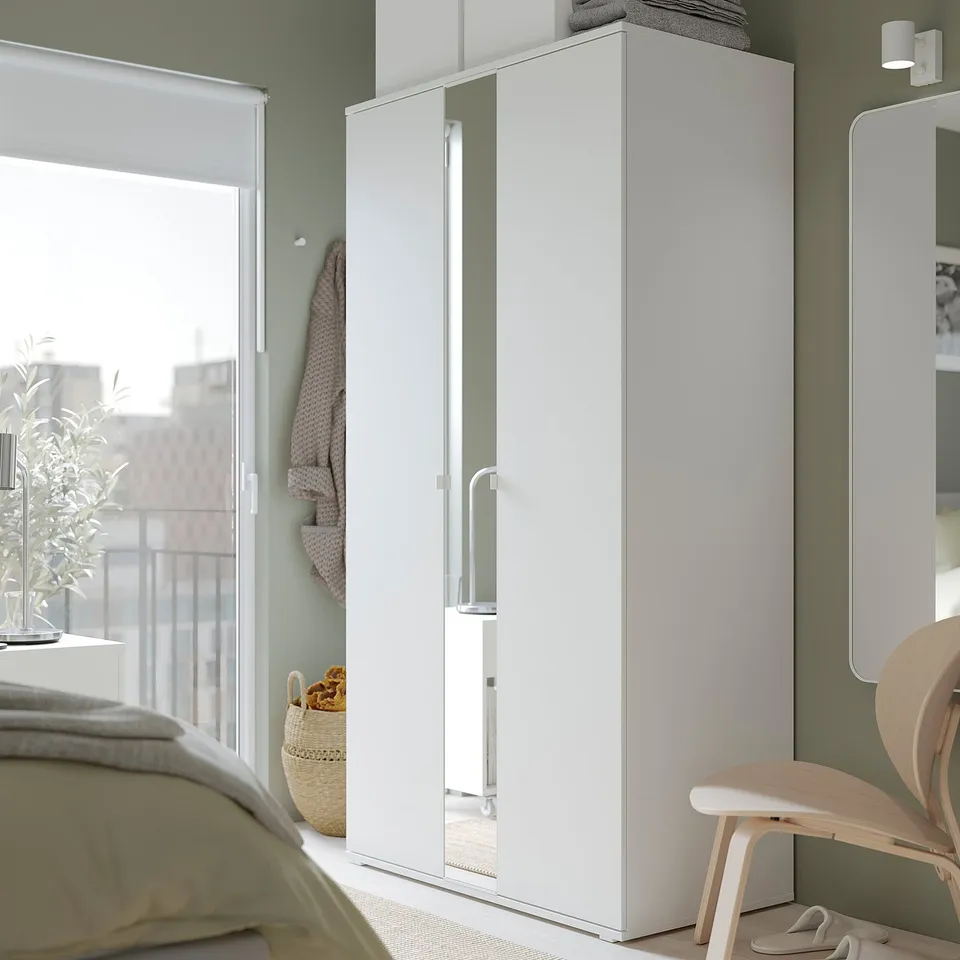 Modern bedroom with white VIHALS wardrobes, full-length mirror, light green walls, and wooden chair.