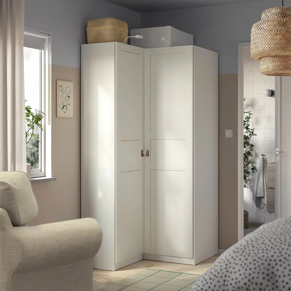 White IKEA PAX closet in room corner, narrow between couch and doorway, double doors with baskets on top shelf.