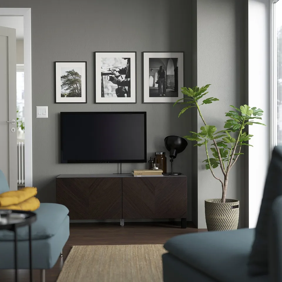 Modern living room with grey walls, BESTÅ tv console, photos, green plant, blue chairs with yellow blanket.