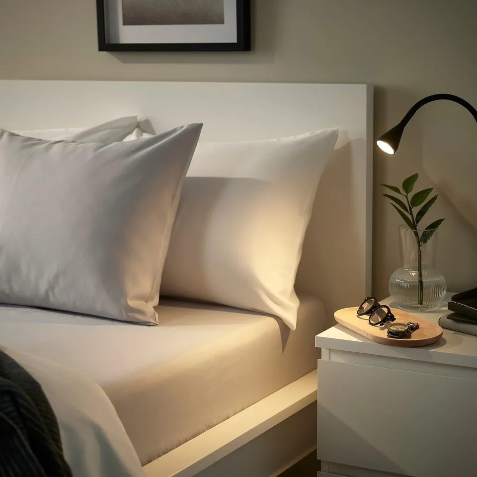 Bed with grey BÄRGLIM fitted sheet on a white bed frame. Sheet is soft, made from recycled polyester, and fits mattresses up to 16 cm thick.