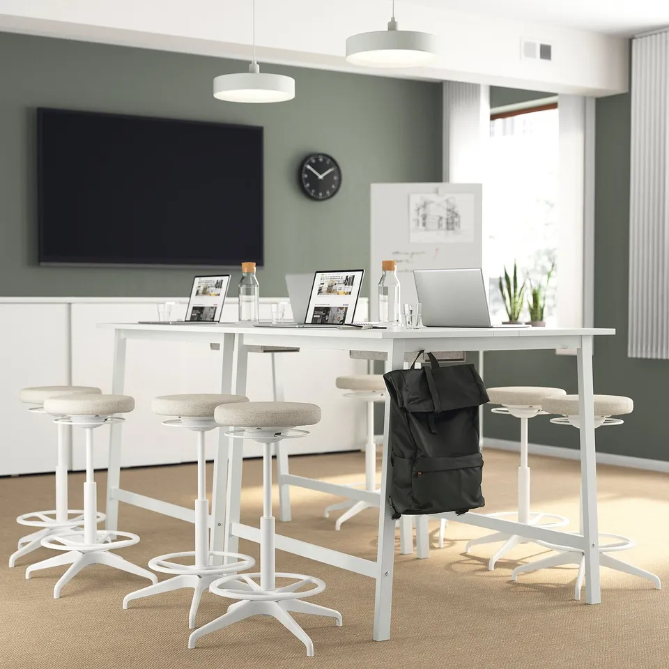Modern office setup with MITTZON white high tables and stools, tv, laptops, and plants.