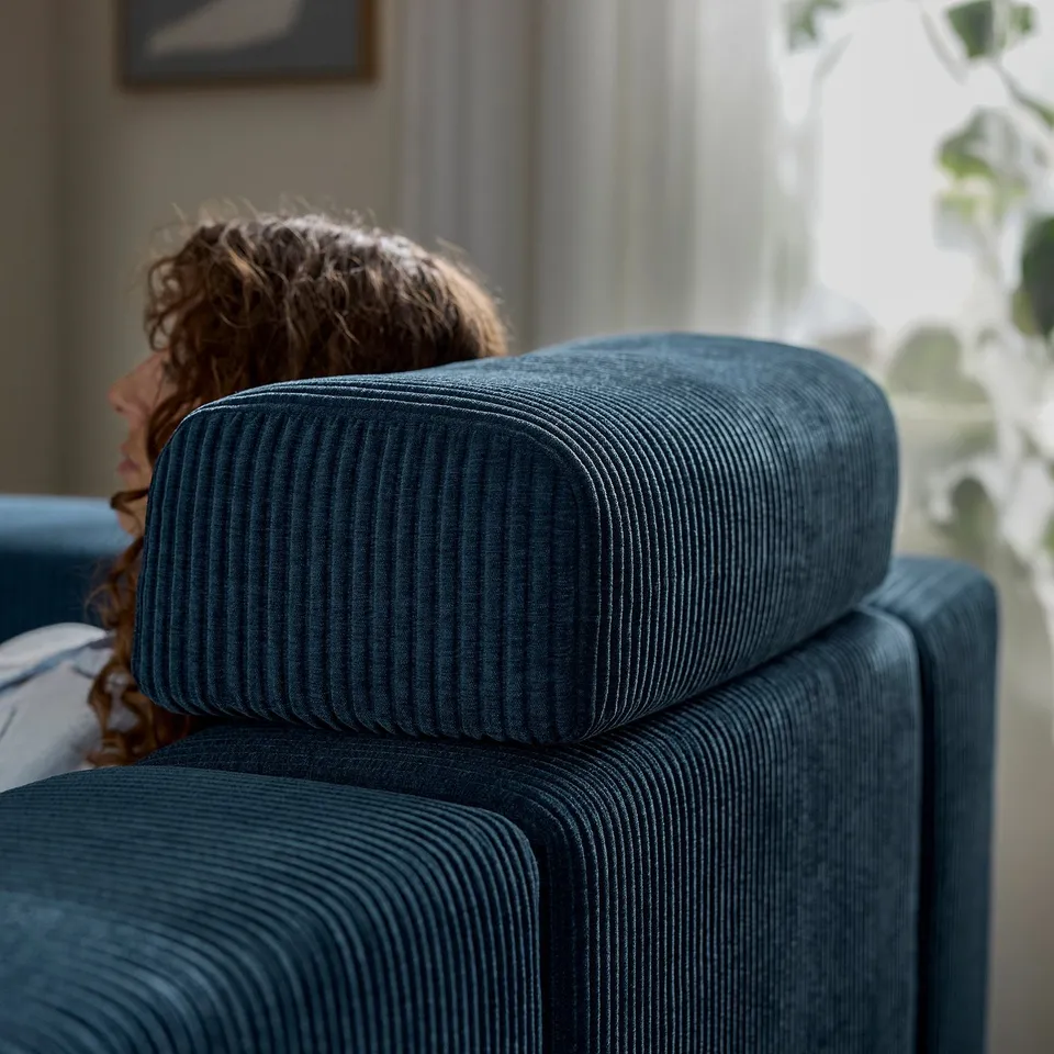 A person resting on a blue JÄTTEBO sofa, utilising the supportive headrest cushion.