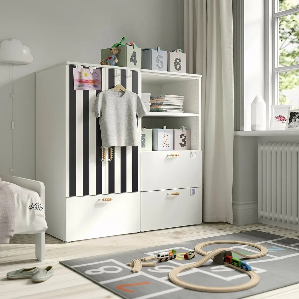 Childs room with SMÅSTAD wardrobe, books, drawers, clothes, near window with curtains and toy train.