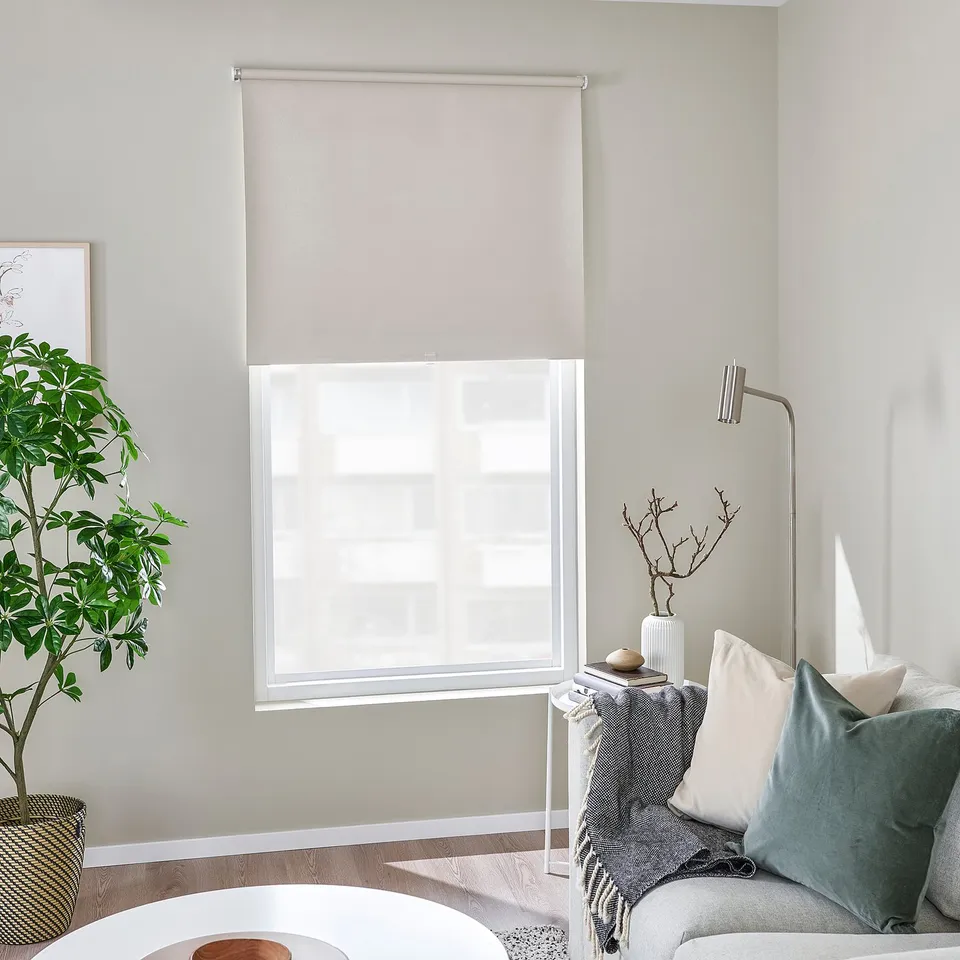Modern room: large window with beige FÖNSTERBLAD blind, grey sofa, plant, frame, lamp, cosy decor.