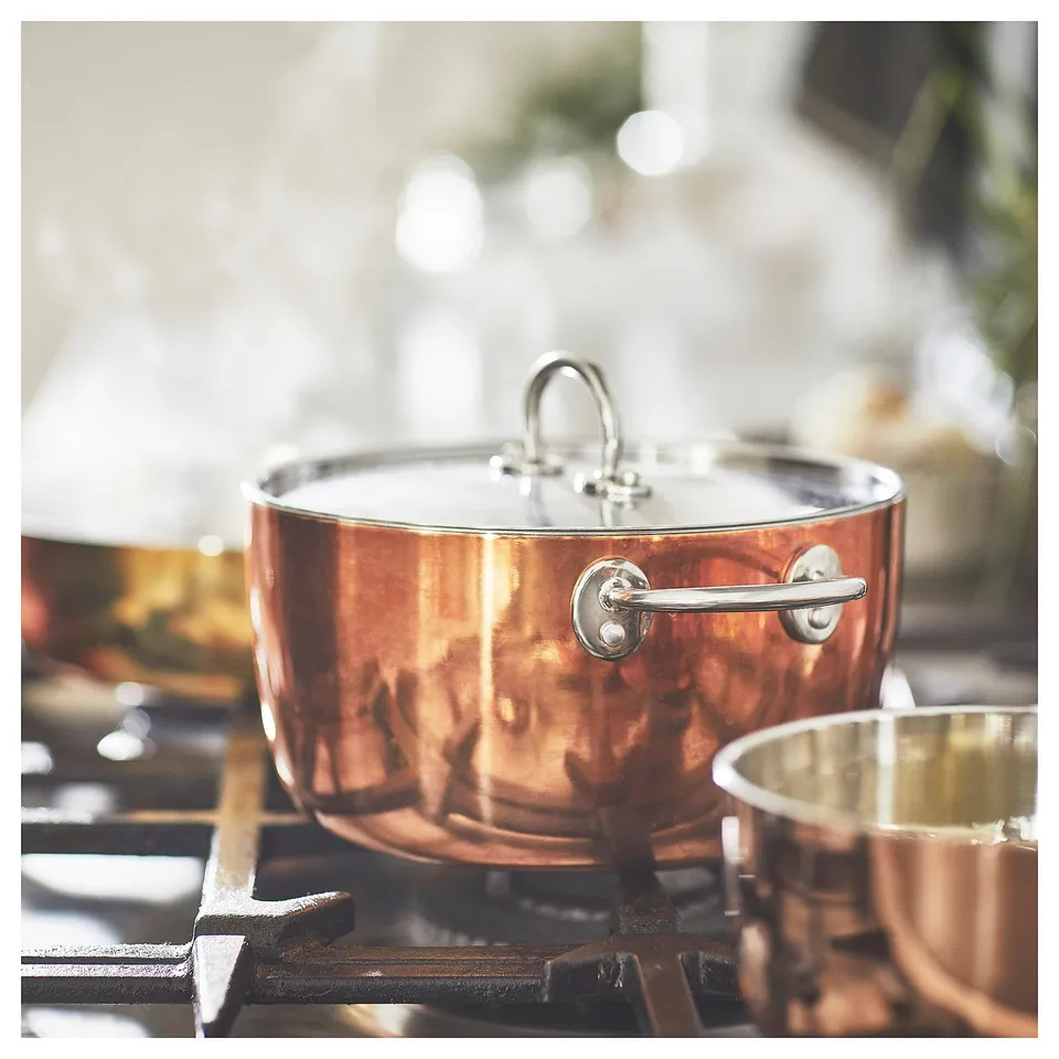 FINMAT copper cookware shines on a gas stove. Round, shiny with a stainless handle and lid, its both functional and stylish.