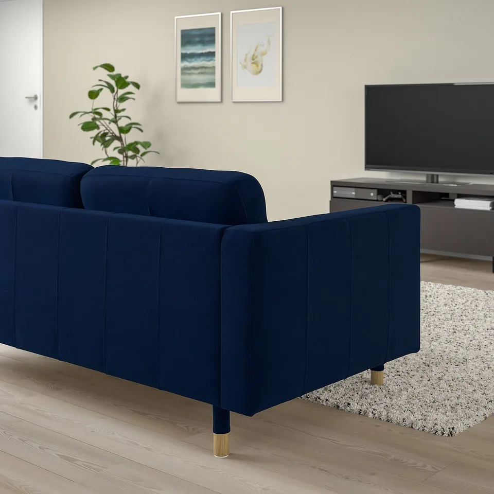 Modern living room with large blue velvet sofa, flat-screen tv, and plant.